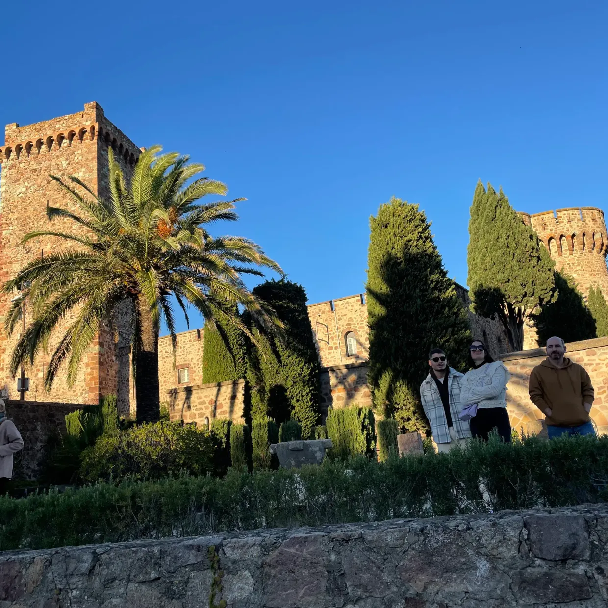 Quatre personnes posent devant un château en pierre entouré d'arbres et de végétation