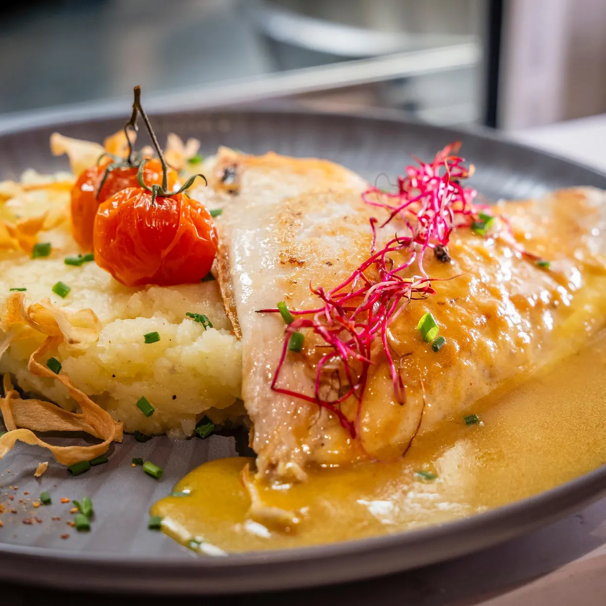 Un filet de poisson grillé posé sur une purée et accompagné de tomates cerises, de radis et de chips de légumes