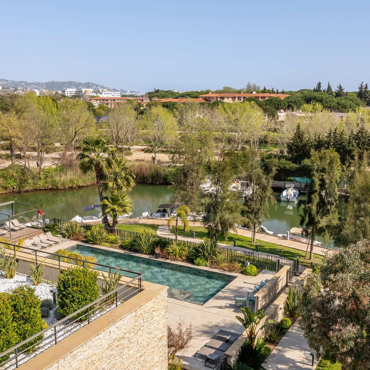 Vue aérienne d'un jardin avec piscine, bordé d'arbres et d'un plan d'eau où sont amarrés des bateaux
