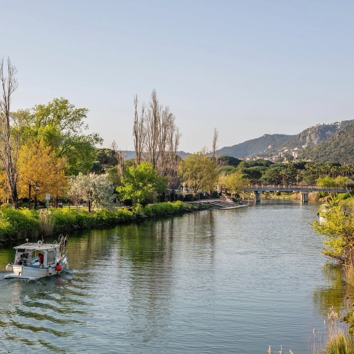 Un bateau navigue sur une rivière bordée d'arbres et de collines, avec un pont visible au loin