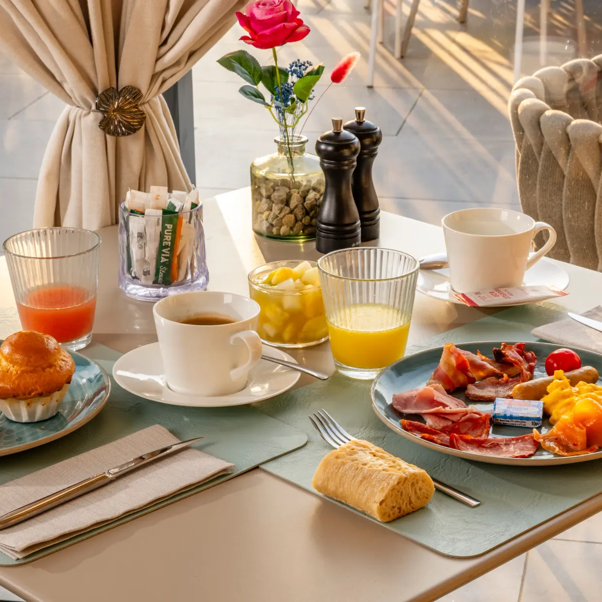 Table dressée pour le petit-déjeuner avec des croissants, des muffins, des œufs, du jambon, du fromage, des boissons et des condiments