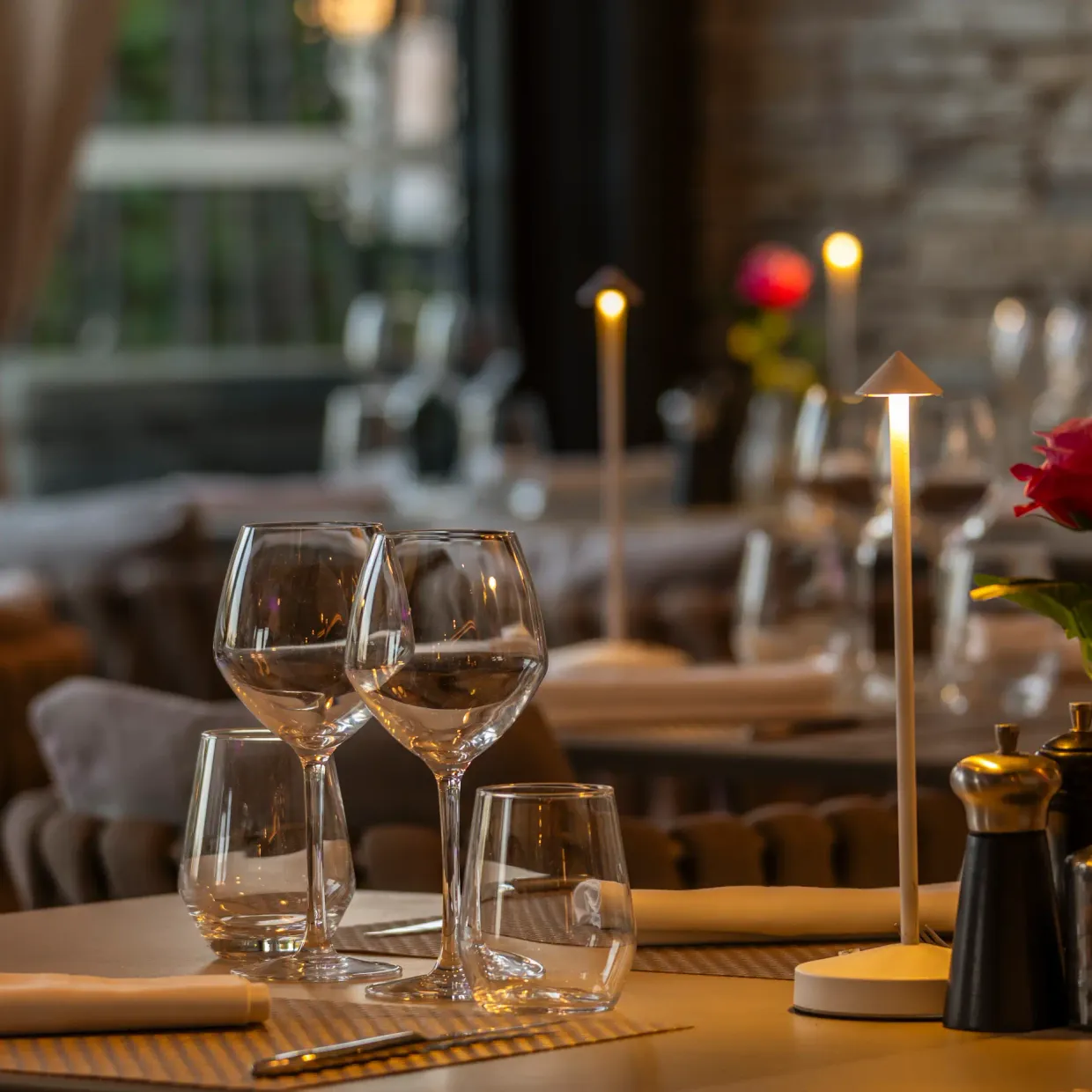 Table dressée avec verres, nappe, rose rouge et bougies dans un restaurant à l'ambiance tamisée