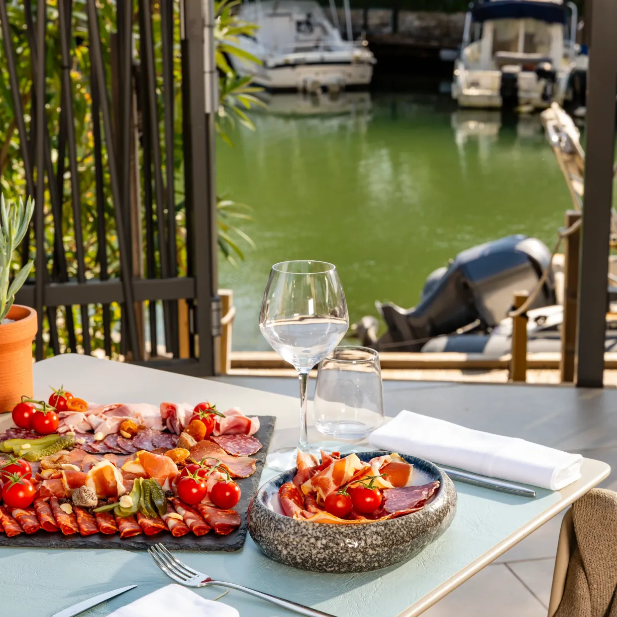 Table avec assiette de charcuterie, verre de vin et vue sur un canal avec des bateaux