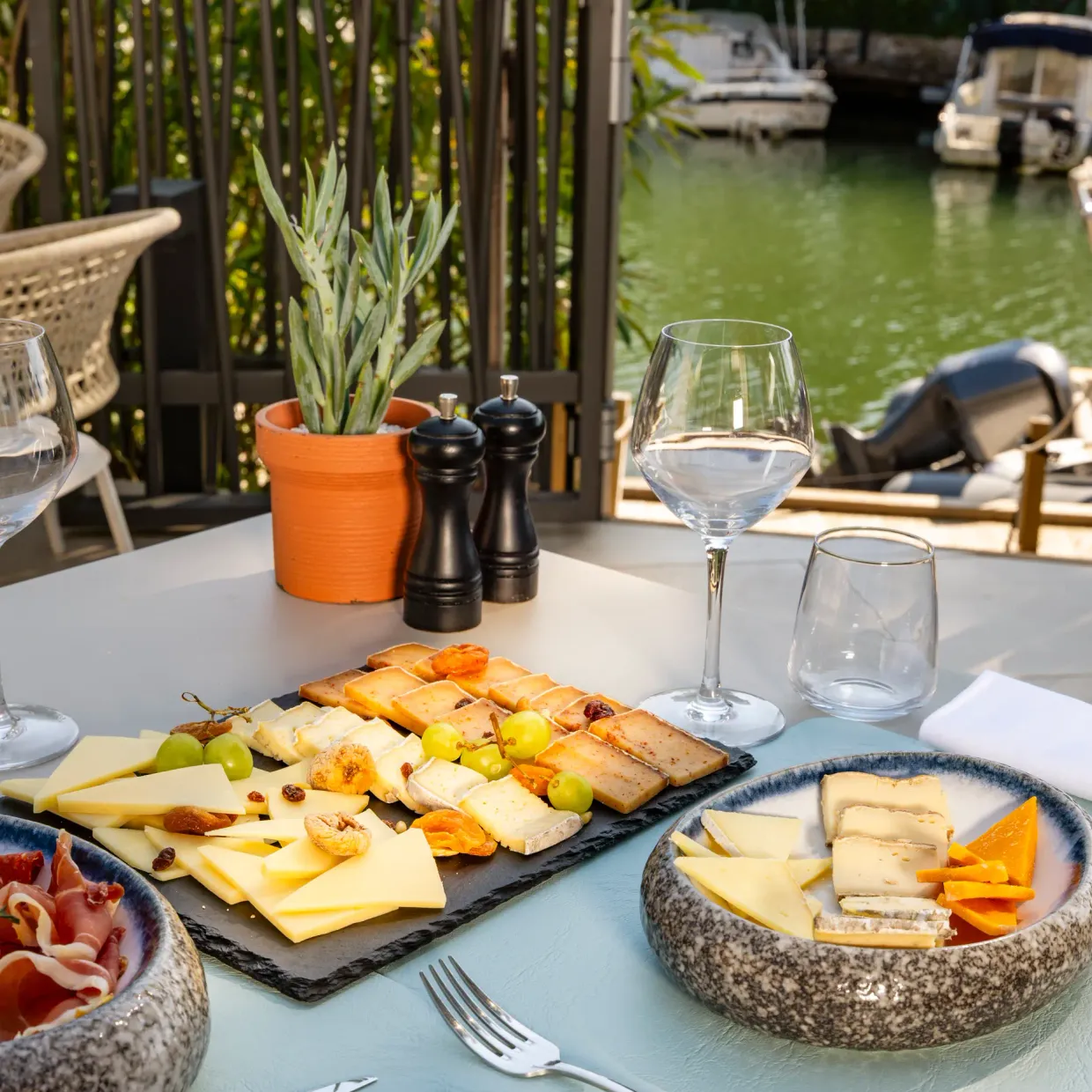 Table avec assiette de charcuterie, fromages, verres et vue sur un canal avec des bateaux