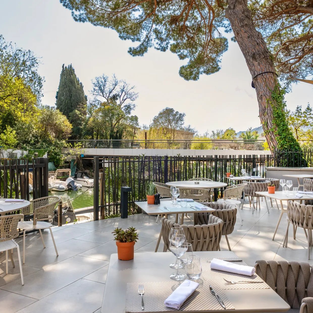 Terrasse de restaurant avec tables et chaises disposées sous une pergola, entourée d'arbres et de verdure