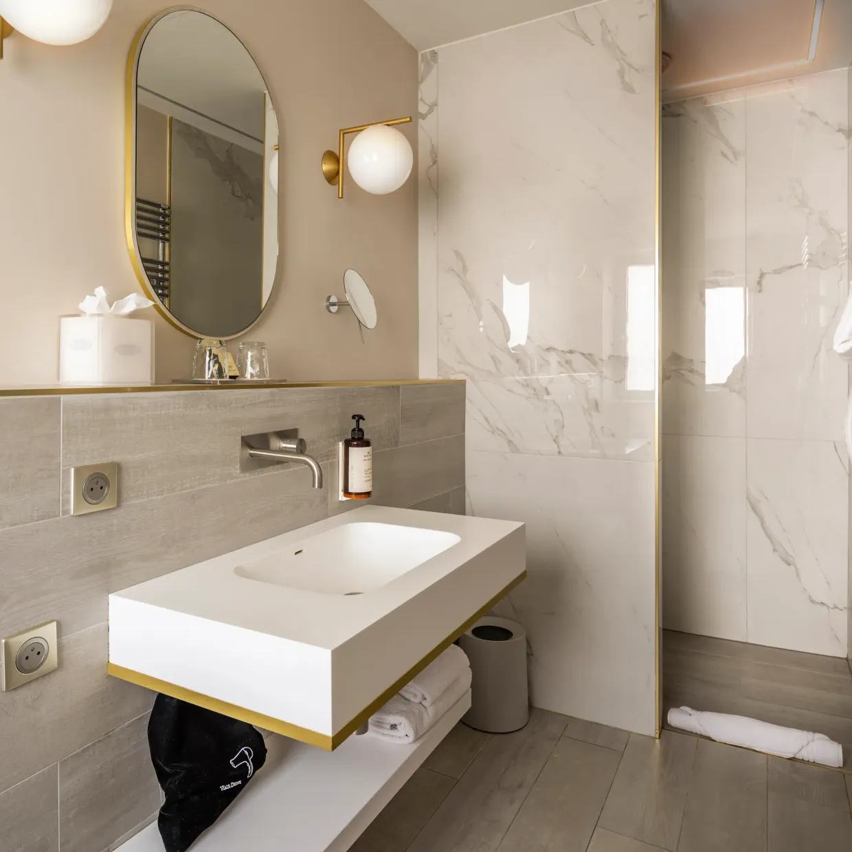 Salle de bain moderne avec lavabo suspendu, miroir ovale, douche à la porte vitrée et serviettes accrochées