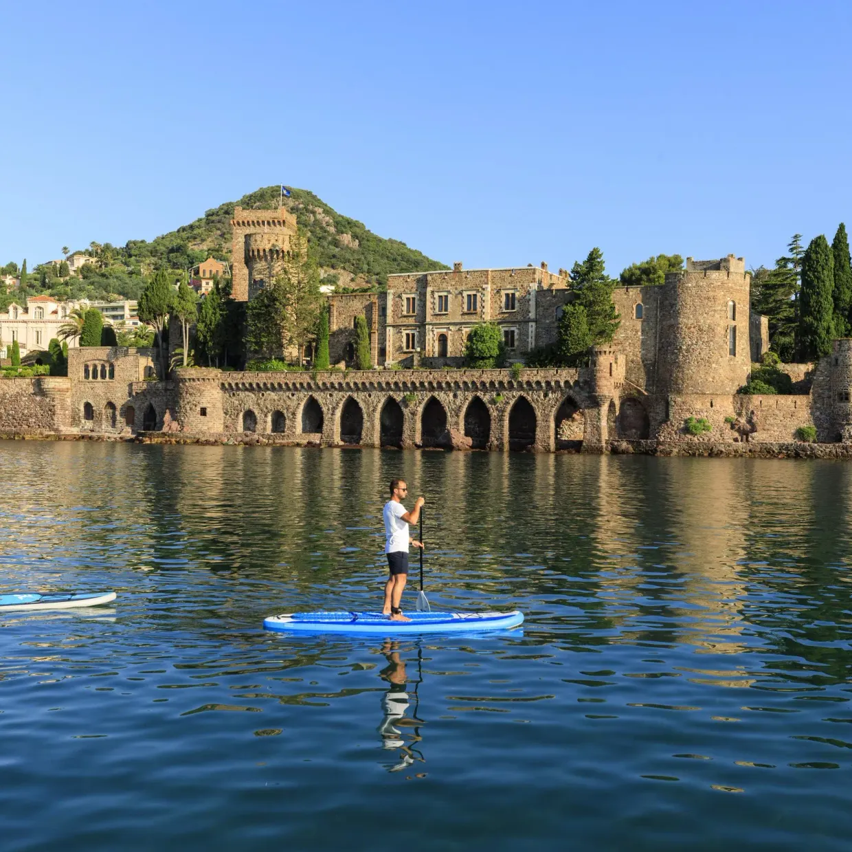 Deux personnes font du paddle sur une étendue d'eau devant un château médiéval entouré de verdure