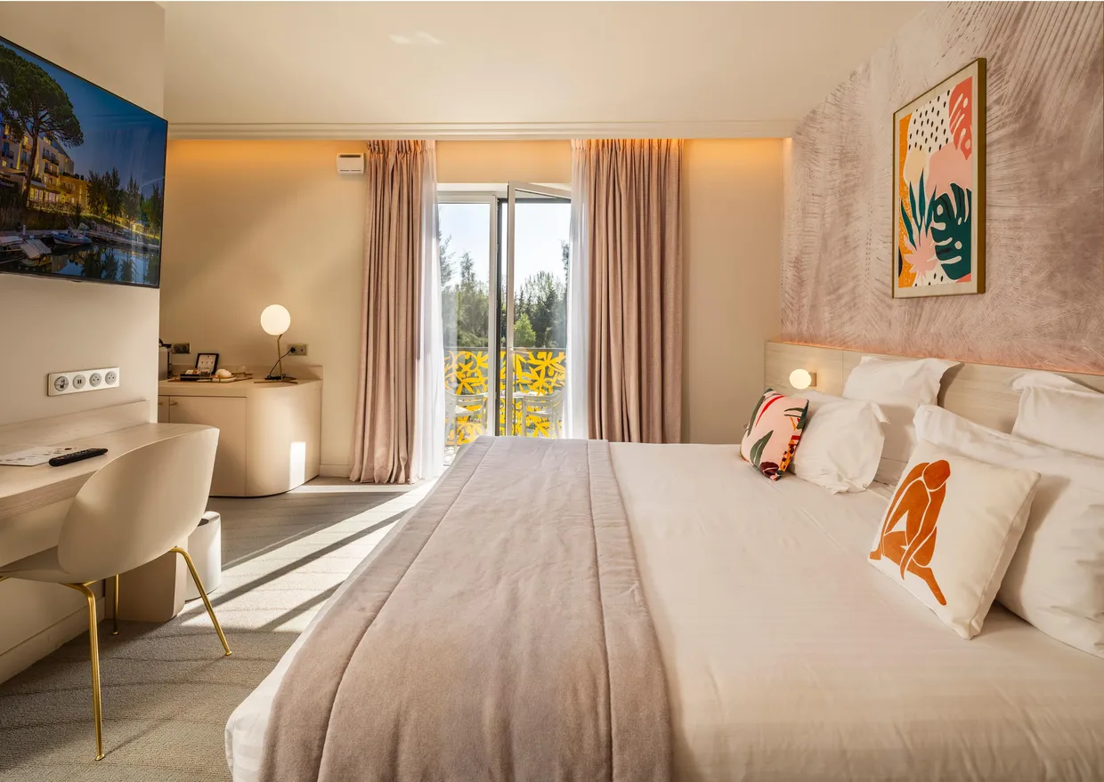 Chambre d'hôtel avec un grand lit, une table de travail, des œuvres d'art sur les murs et une porte-fenêtre donnant sur un balcon
