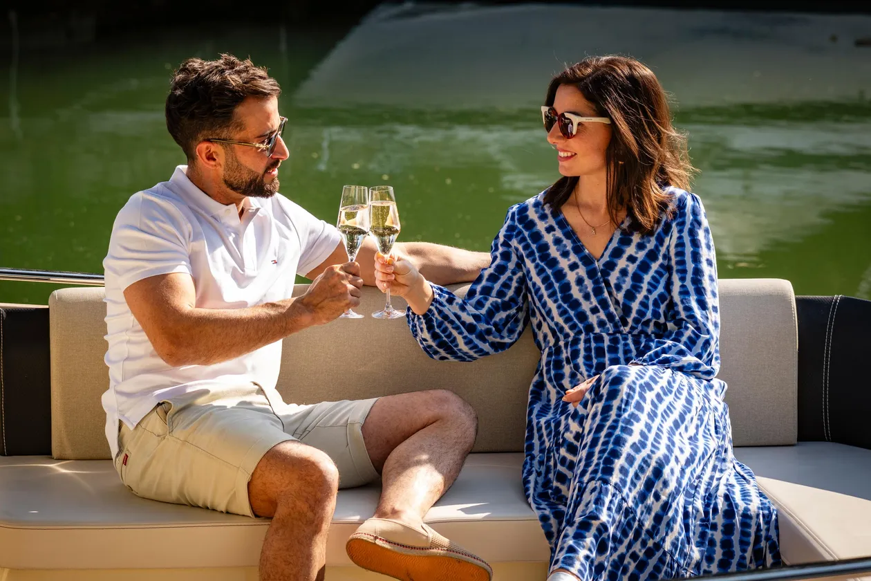 Un homme et une femme assis sur un canapé extérieur lèvent leurs verres de champagne pour trinquer