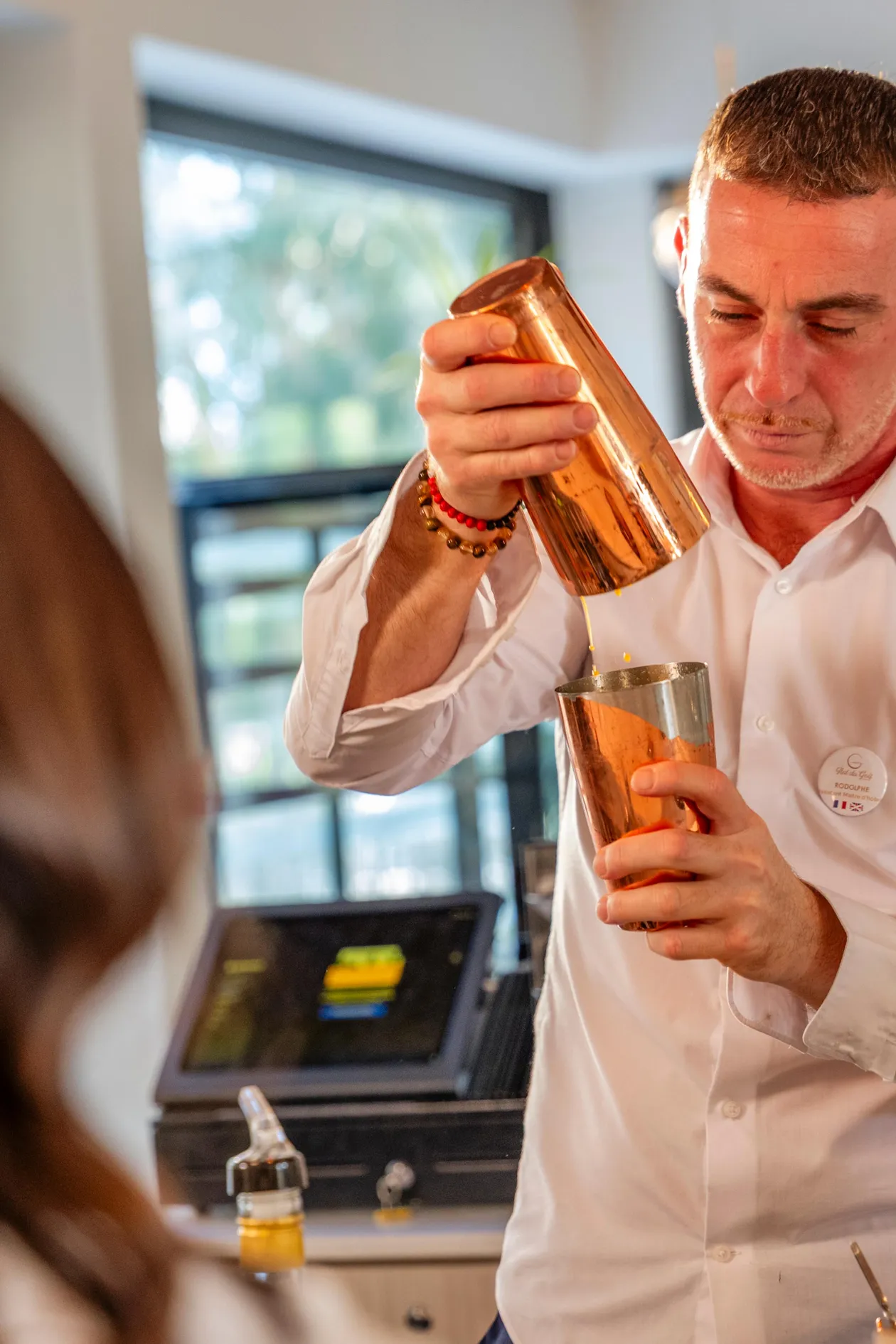 Un homme en chemise blanche prépare un cocktail en versant un liquide d'un shaker métallique dans un verre
