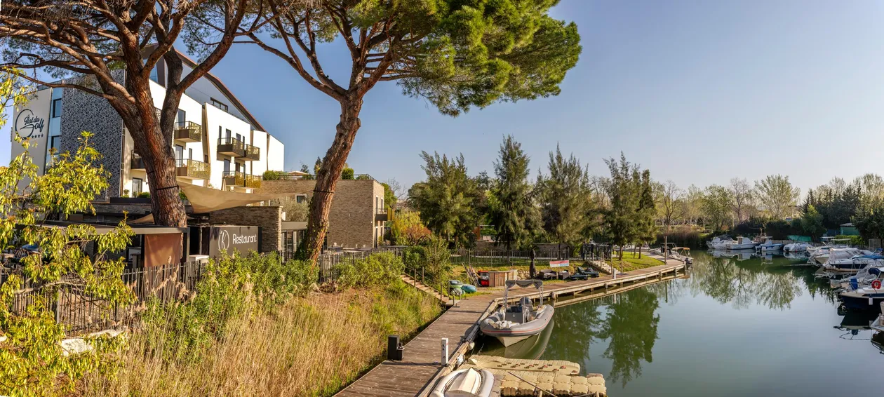 Un hôtel et un restaurant bordent un canal avec des bateaux amarrés, entourés d'arbres et de végétation