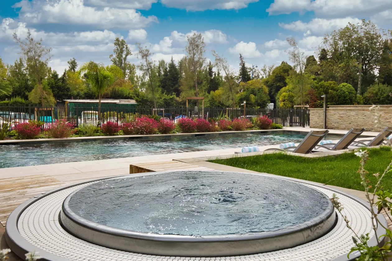 Piscine entourée de chaises longues et de végétation avec un petit bassin circulaire au premier plan