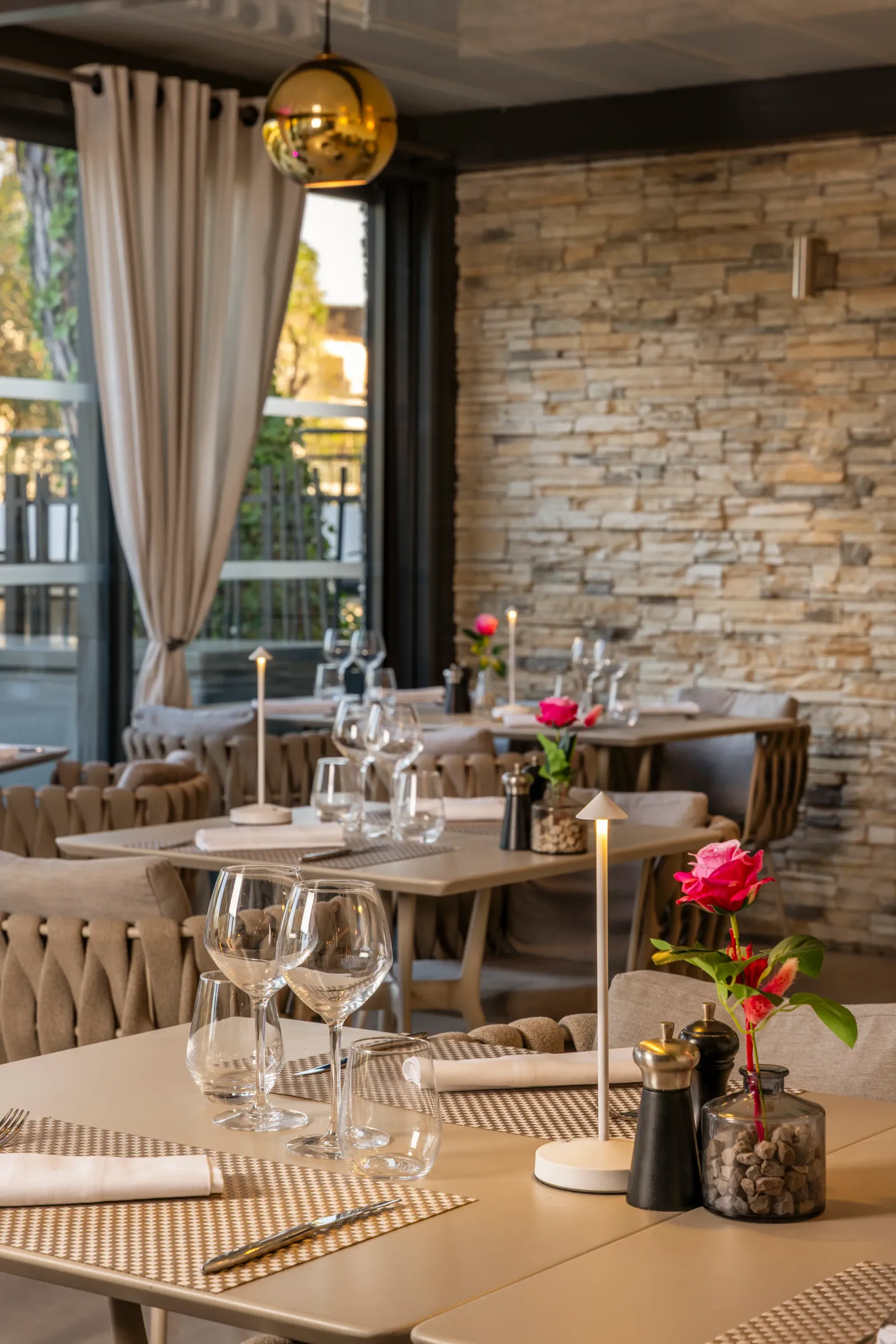 Table dressée dans un restaurant avec verres à vin, serviettes, fleurs et pierre à sel, devant un mur en pierre et une fenêtre avec des rideaux