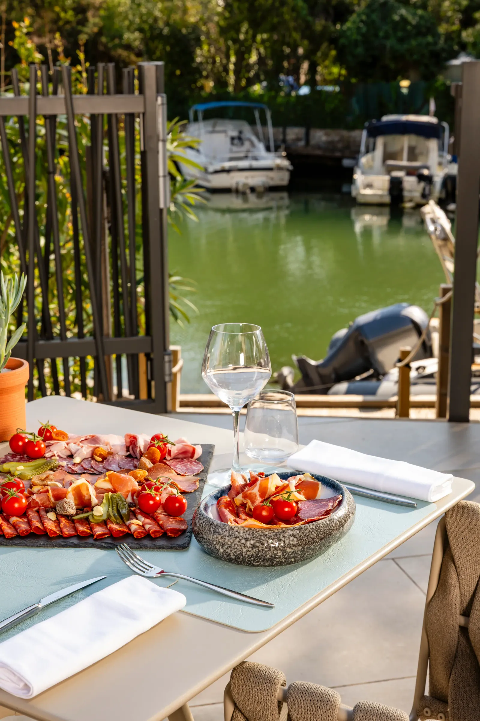 Table avec assiette de charcuterie, verre de vin et vue sur un canal avec des bateaux