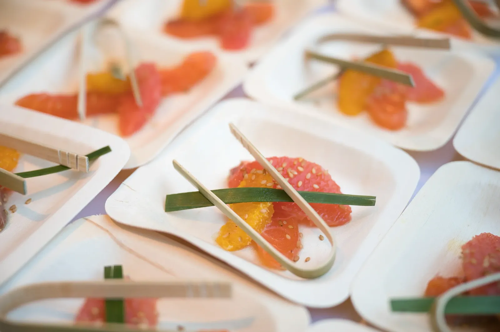 Petits plats en carton contenant des morceaux de fruits et des bâtonnets, disposés sur une nappe à motifs