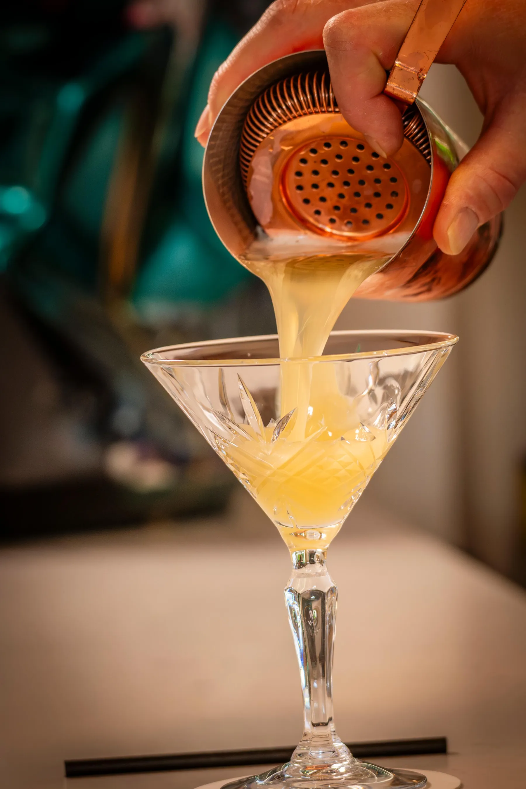 Un liquide jaune est versé dans un verre à martini à l'aide d'un tamis à cocktail