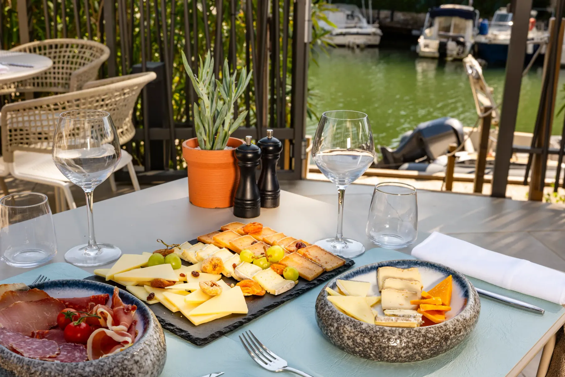 Table avec assiette de charcuterie, fromages, verres et vue sur un canal avec des bateaux