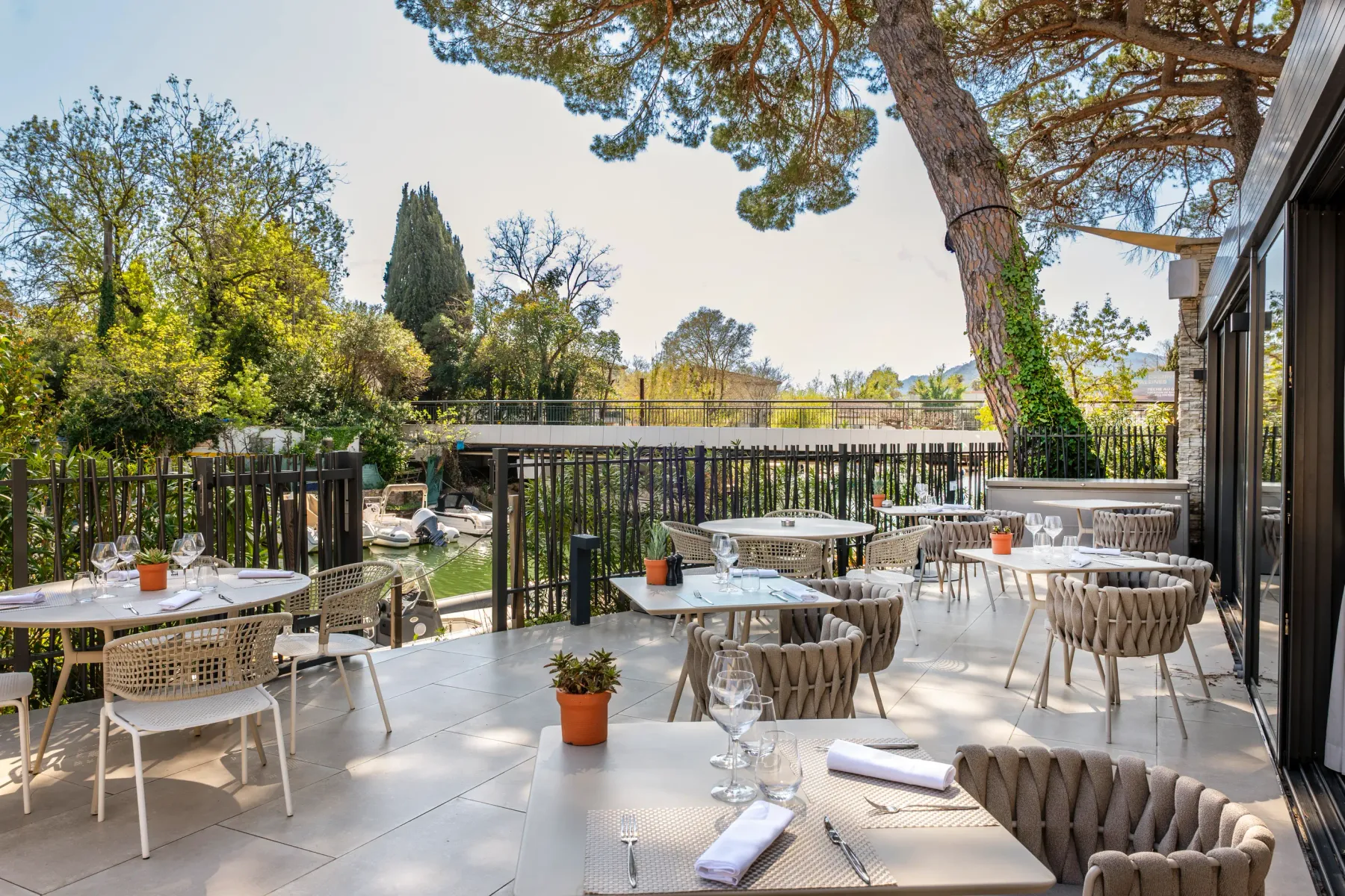 Terrasse de restaurant avec tables et chaises disposées sous une pergola, entourée d'arbres et de verdure