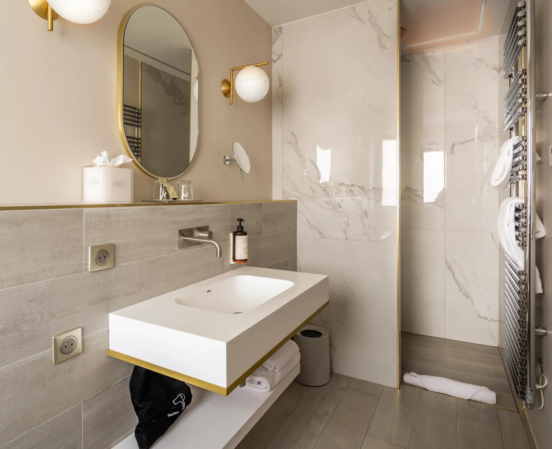 Salle de bain moderne avec lavabo suspendu, miroir ovale, douche à la porte vitrée et serviettes accrochées