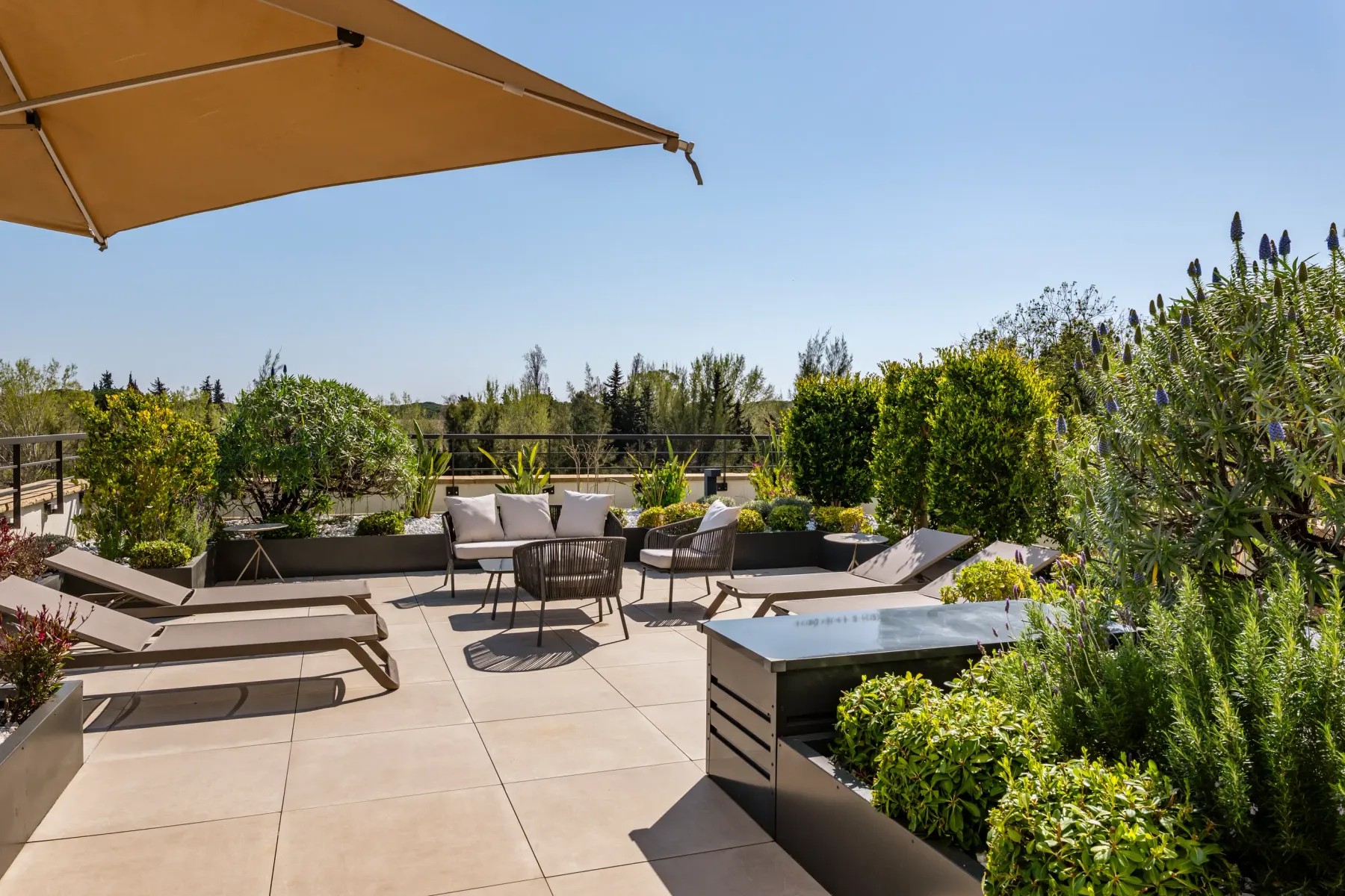 Terrasse avec des chaises longues, un canapé, des plantes et un parasol sous un ciel dégagé