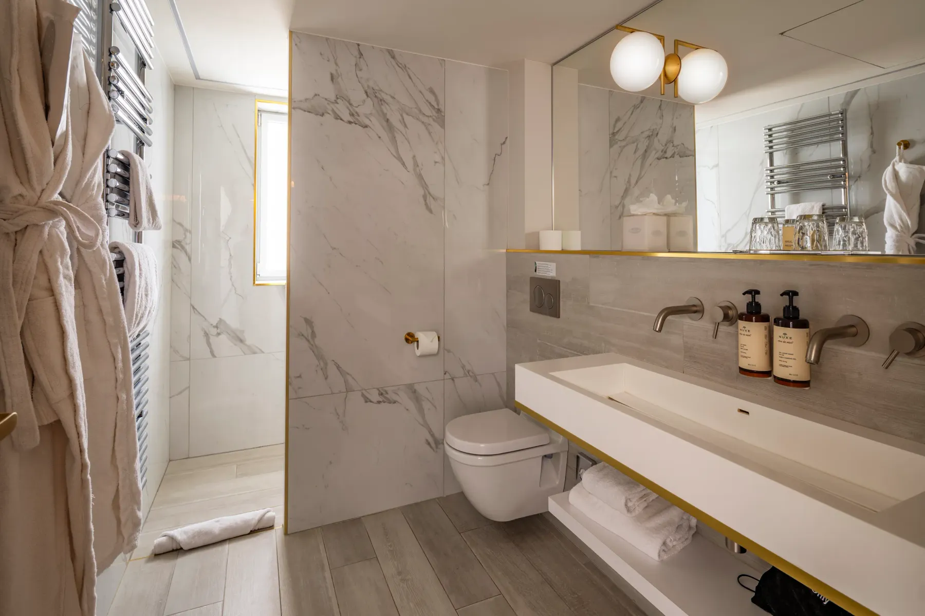 Salle de bain moderne avec lavabo, toilettes, miroir et étagères en marbre, serviettes suspendues et produits de toilette