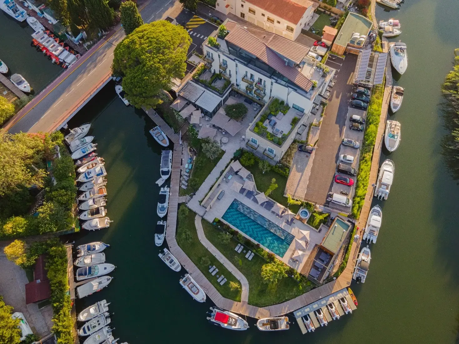 Vue aérienne d'une propriété résidentielle en bord de rivière avec piscine, bateaux amarrés et voitures garées