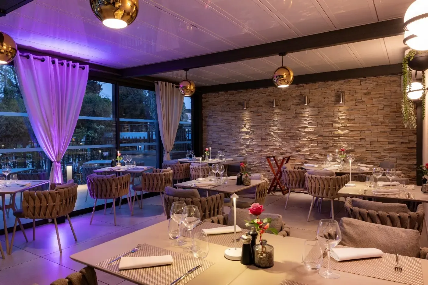 Restaurant élégant avec tables dressées, chaises rembourrées et lumières tamisées, vue sur l'extérieur à travers de grandes baies vitrées