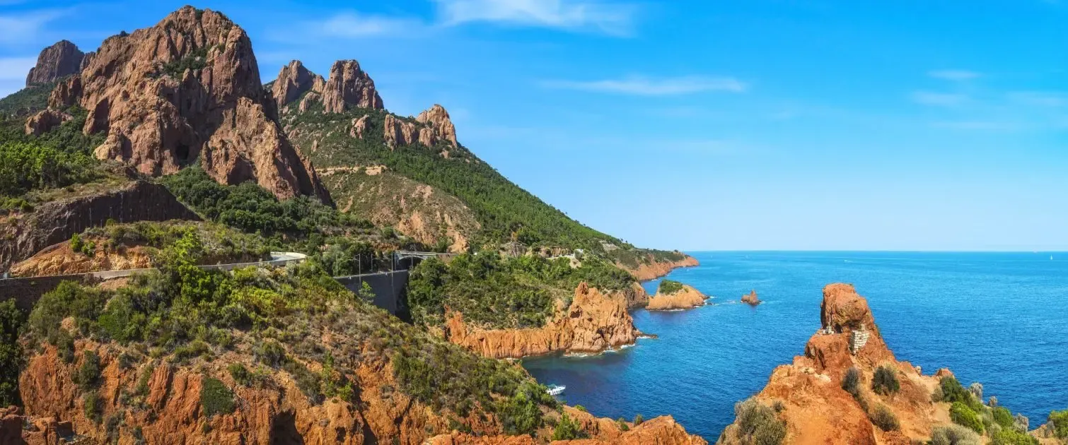 Une côte rocheuse avec des formations montagneuses escarpées et une route sinueuse longeant la mer bleue sous un ciel dégagé