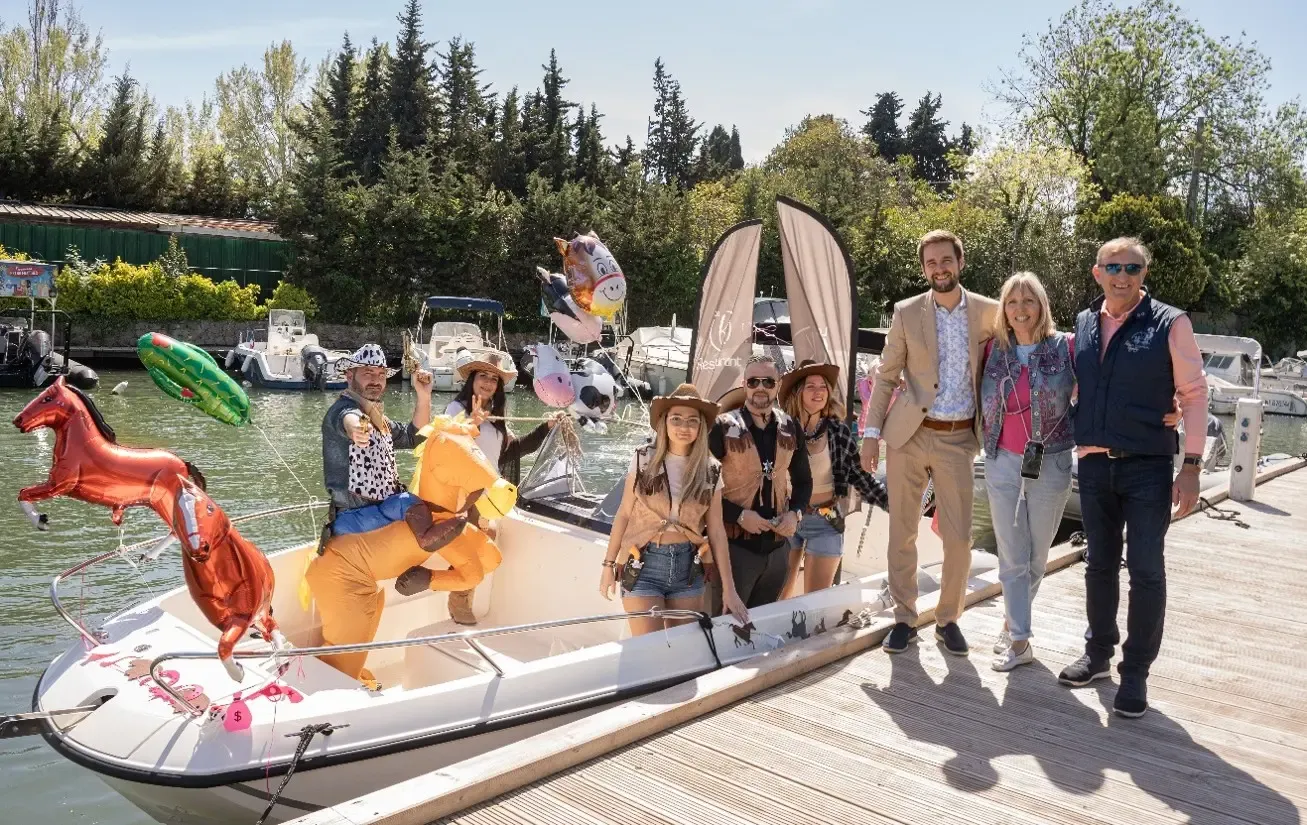 Un groupe de personnes pose sur un bateau décoré de ballons en forme d'animaux, près d'un quai avec des bateaux à l'arrière-plan