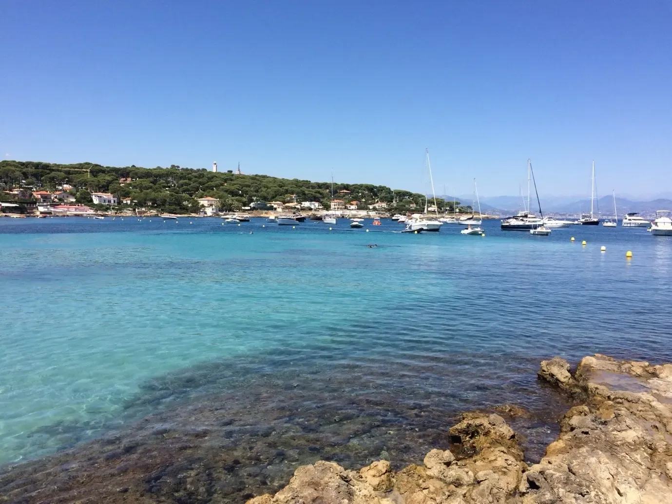 Vue d'une baie avec des eaux turquoise, des bateaux à voile et un village côtier en arrière-plan