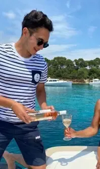 Un homme en t-shirt rayé verse du vin blanc dans un verre sur un bateau à moteur au bord de l'eau