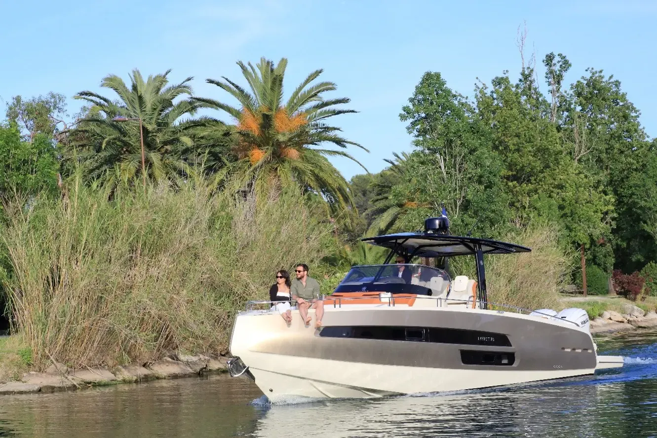 Un bateau blanc avec deux personnes à bord navigue sur une rivière bordée de végétation et de palmiers