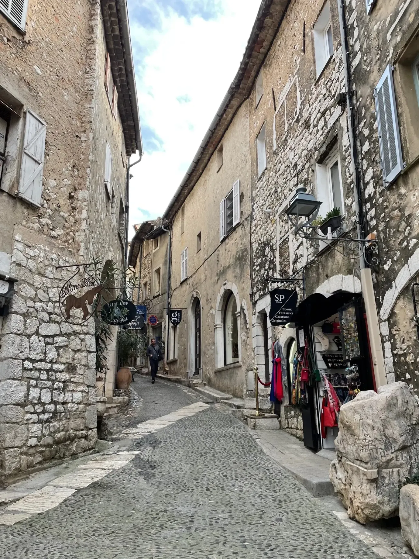 Ruelle pavée bordée de bâtiments en pierre avec des boutiques et une personne marchant au loin