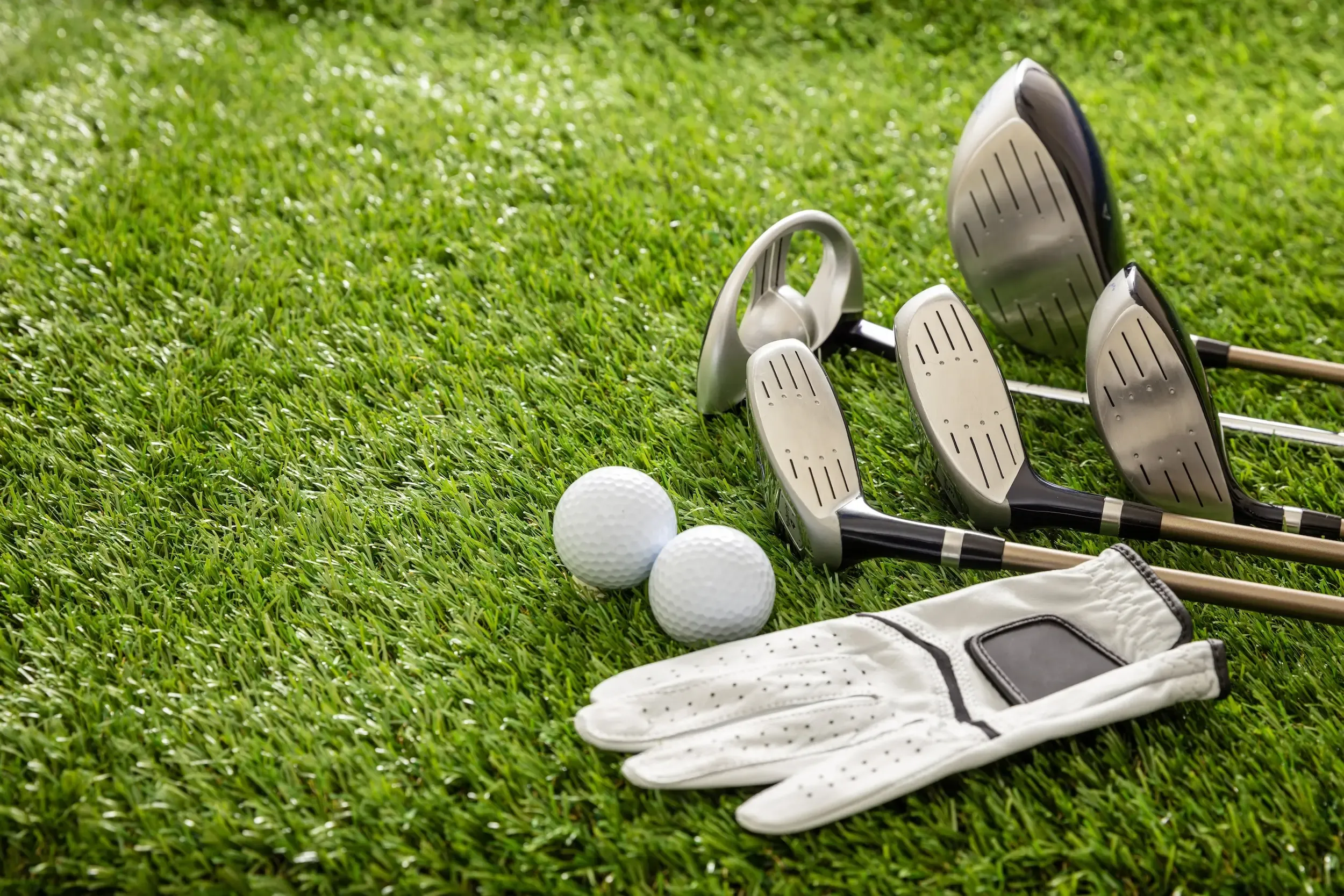 Gants de golf, balles de golf, club de golf et un marqueur de balle posés sur une pelouse verte
