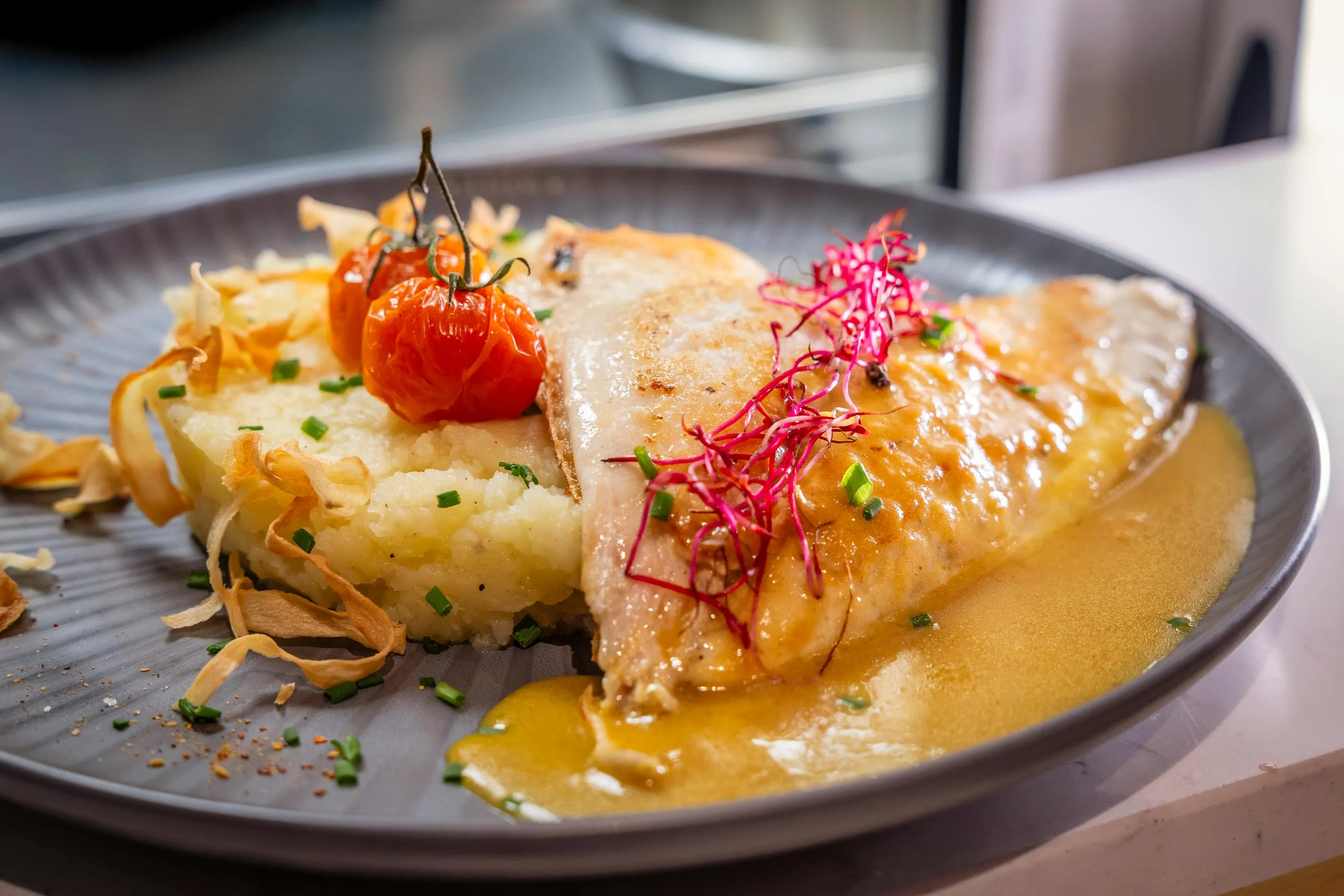 Un filet de poisson grillé posé sur une purée et accompagné de tomates cerises, de radis et de chips de légumes