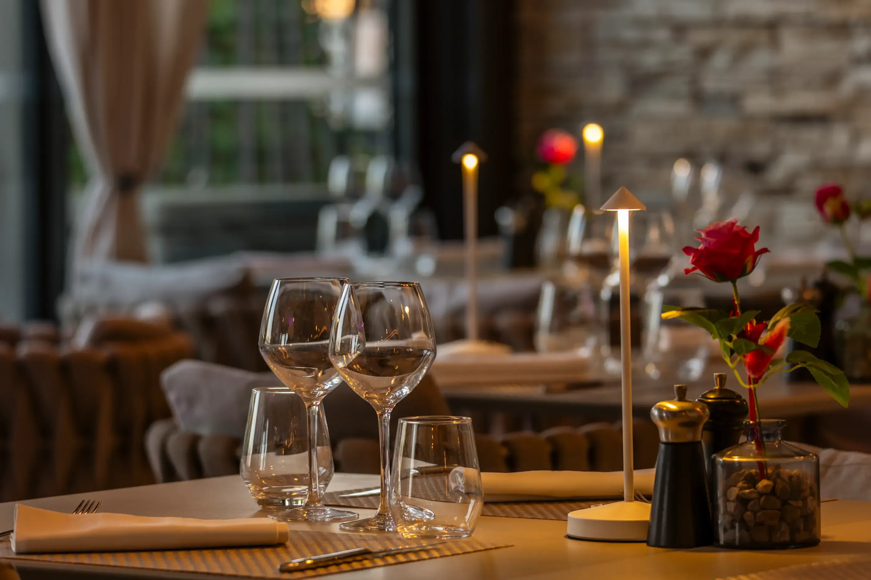 Table dressée avec verres, nappe, rose rouge et bougies dans un restaurant à l'ambiance tamisée