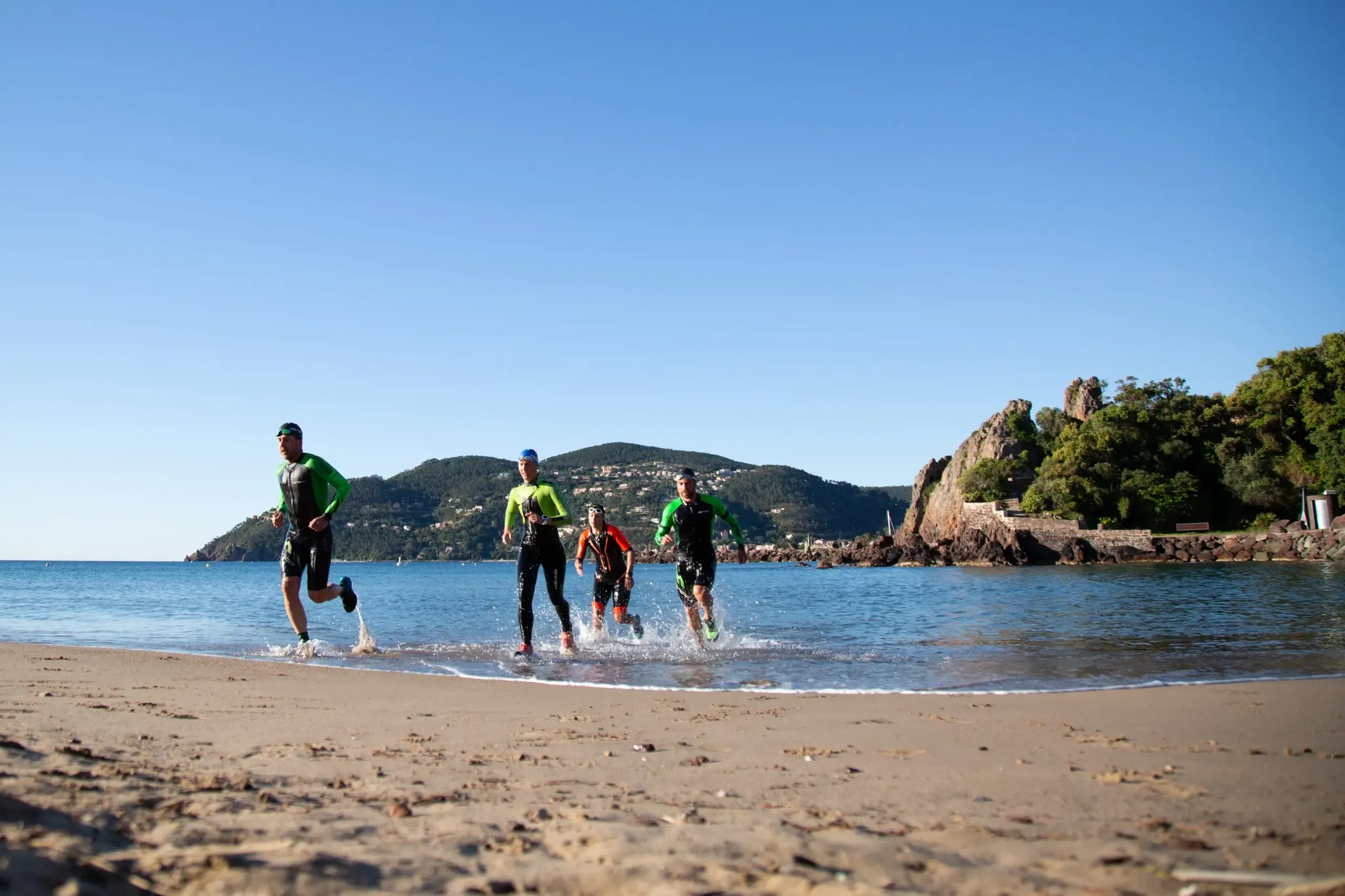 Quatre personnes en tenue de sport courent sur une plage avec des montagnes en arrière-plan