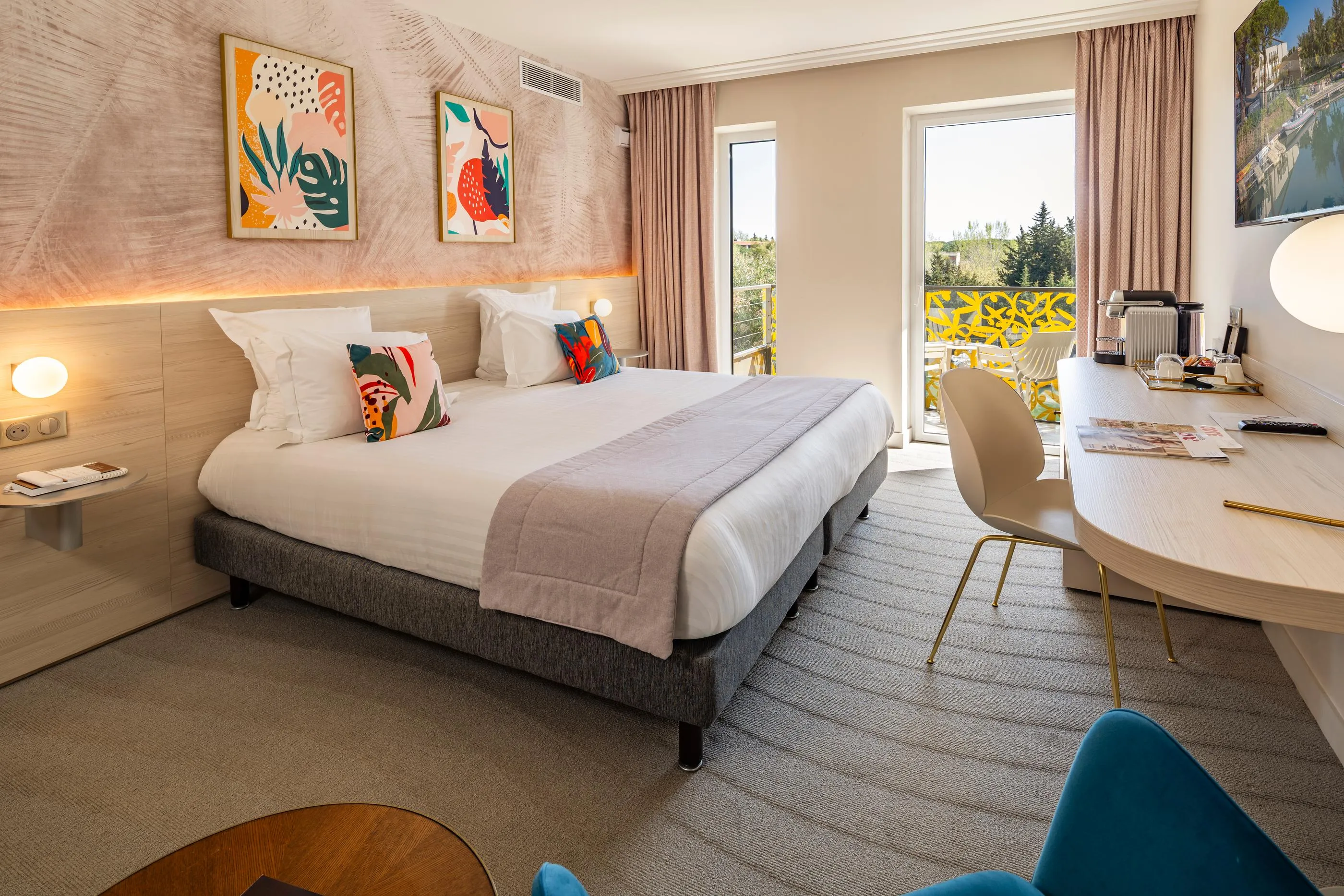 Chambre d'hôtel avec un lit, une table de travail, des œuvres d'art murales et une porte-fenêtre donnant sur un balcon