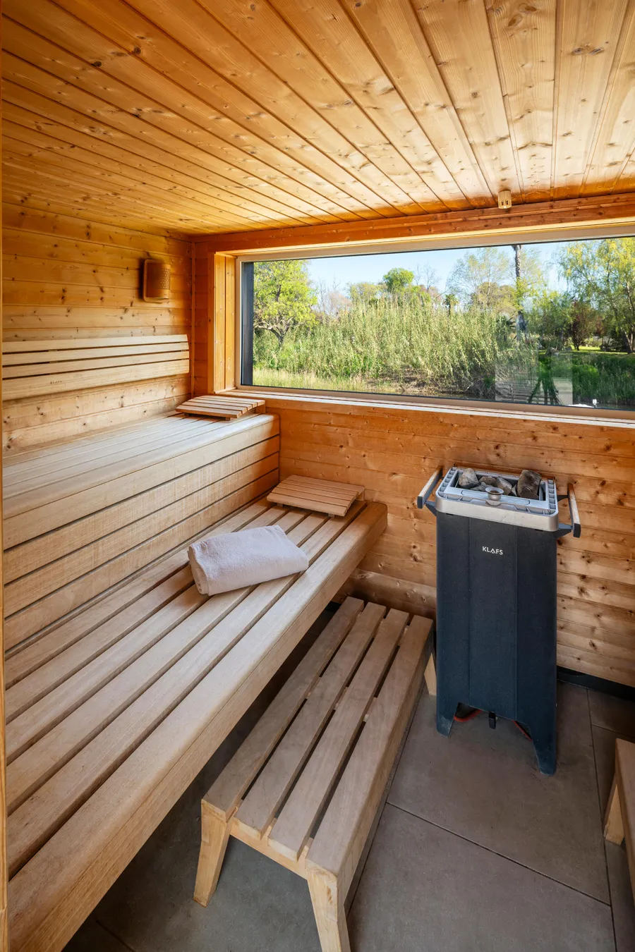 Sauna en bois avec bancs, chauffage électrique et vue sur l'extérieur à travers une fenêtre