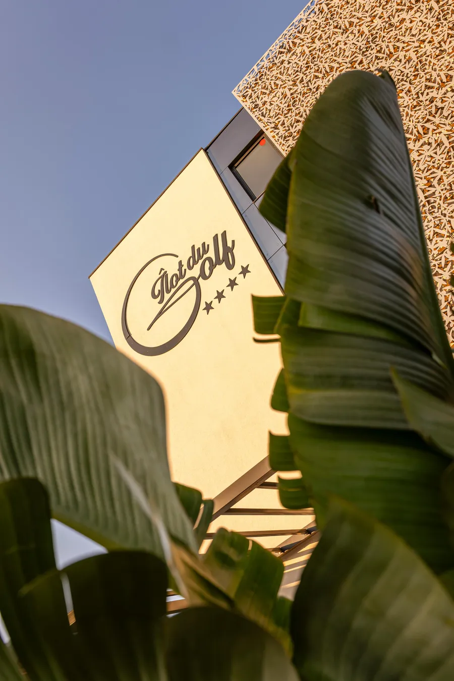 Panneau avec l'inscription "Notre Golf" et trois étoiles, partiellement caché par des feuilles de plantes vertes