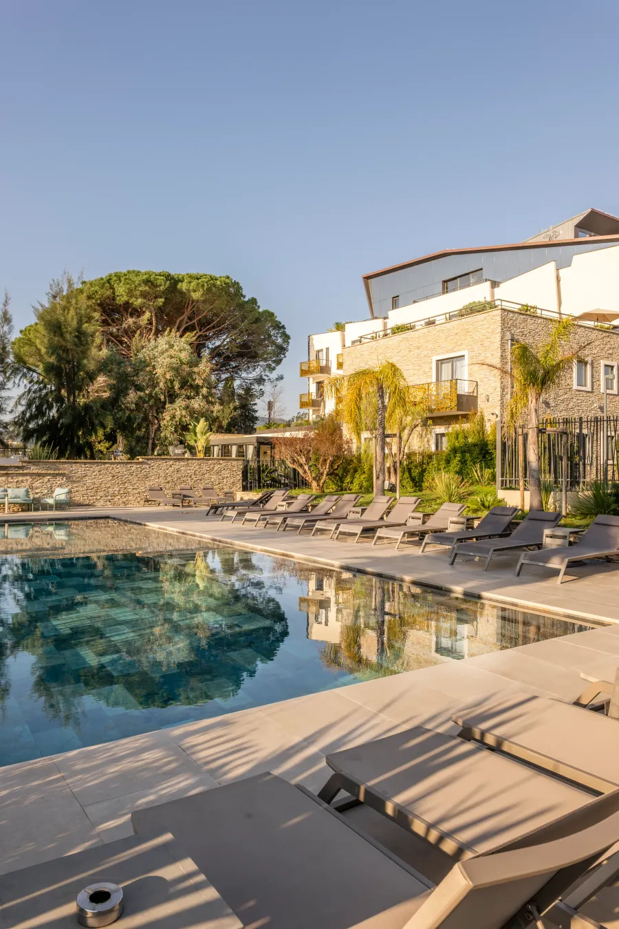 Piscine entourée de transats avec un bâtiment en pierre et des arbres en arrière-plan